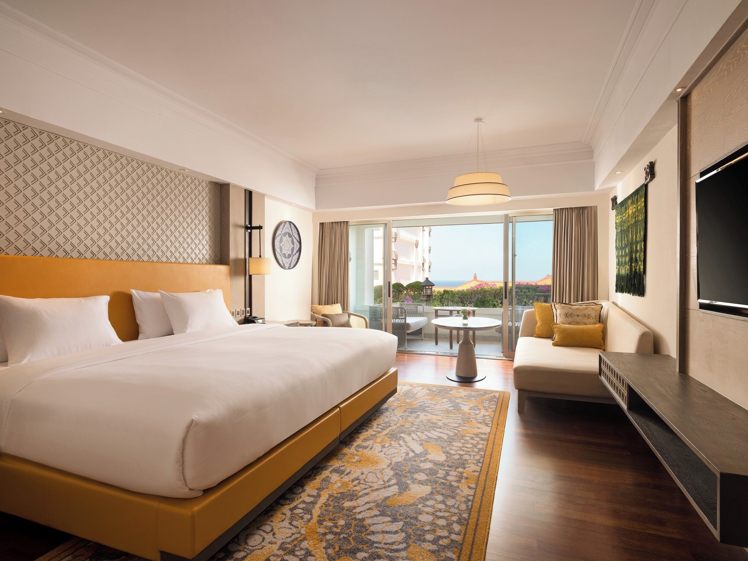 A hotel room with a large bed, a sofa, a TV, and a balcony with a view.