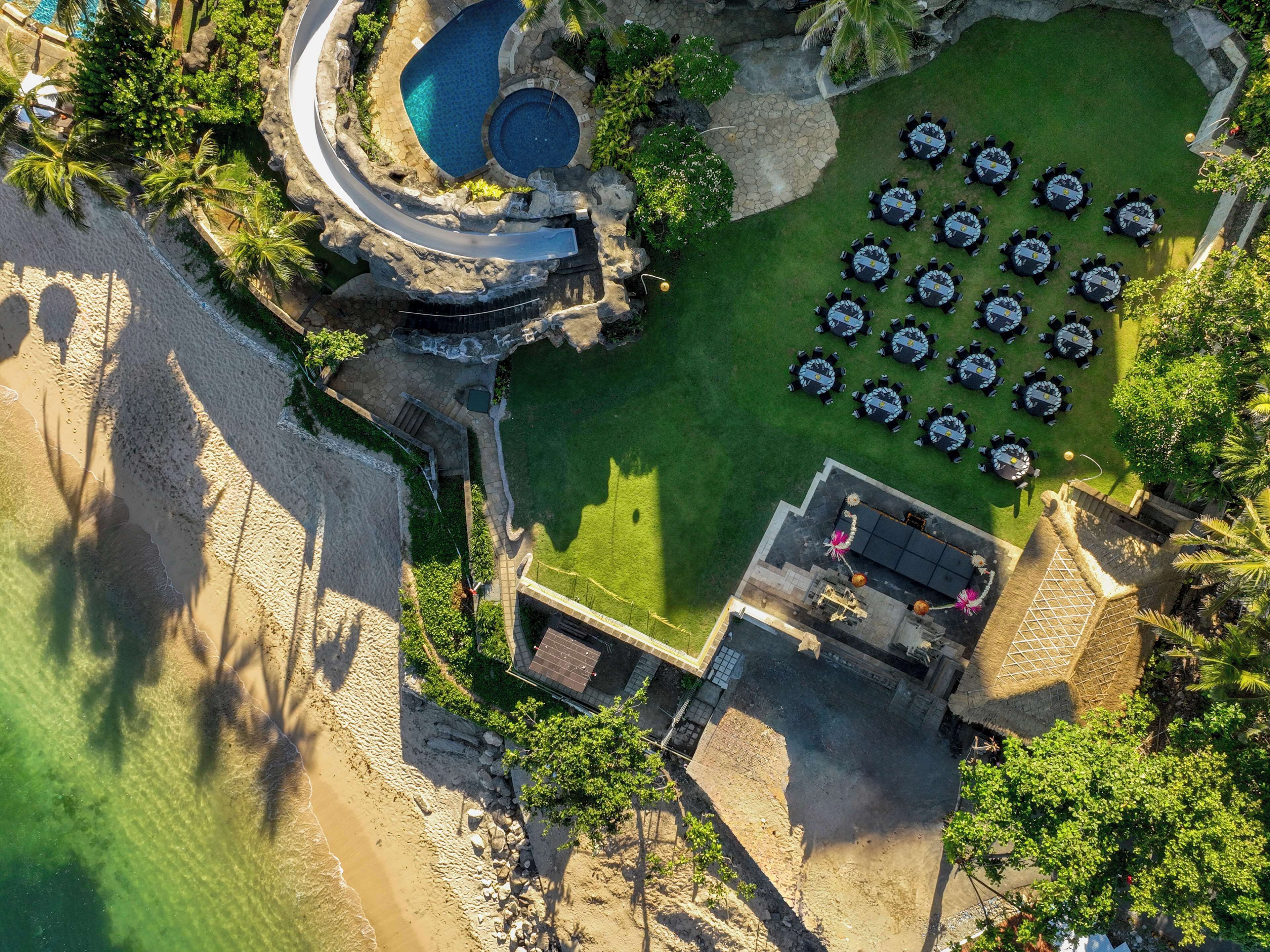 An aerial view of a resort with a swimming pool, beach, and outdoor dining area.