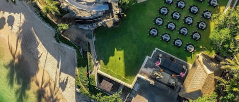 An aerial view of a resort with a swimming pool, beach, and outdoor dining area.