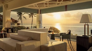Un moderno cuarto de hotel con un ventanal grande con vista al mar, un sofá, una silla y una mesa con una lámpara.