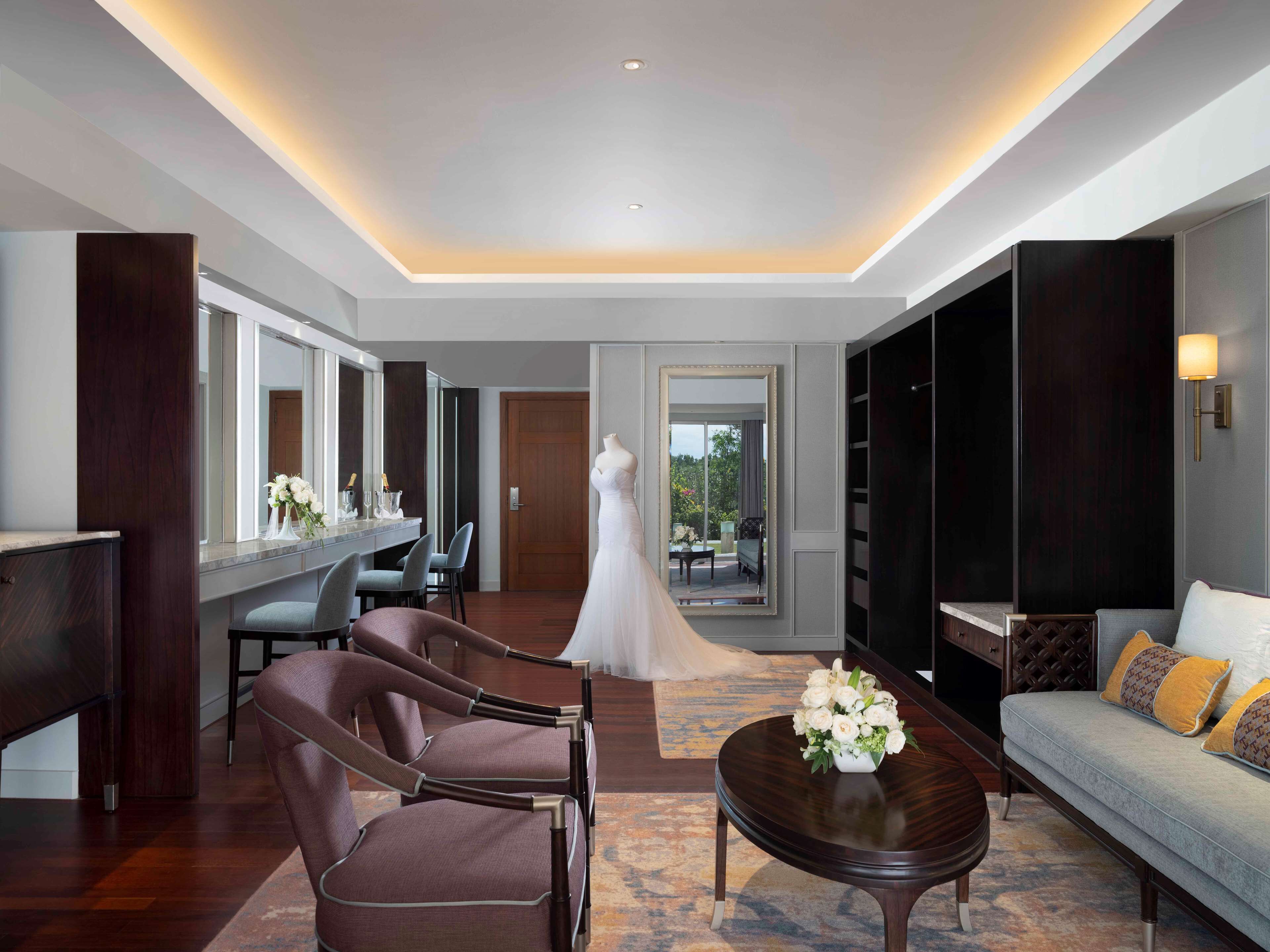 A spacious hotel room with a large mirror, a dress form, a sofa, and a dining area.