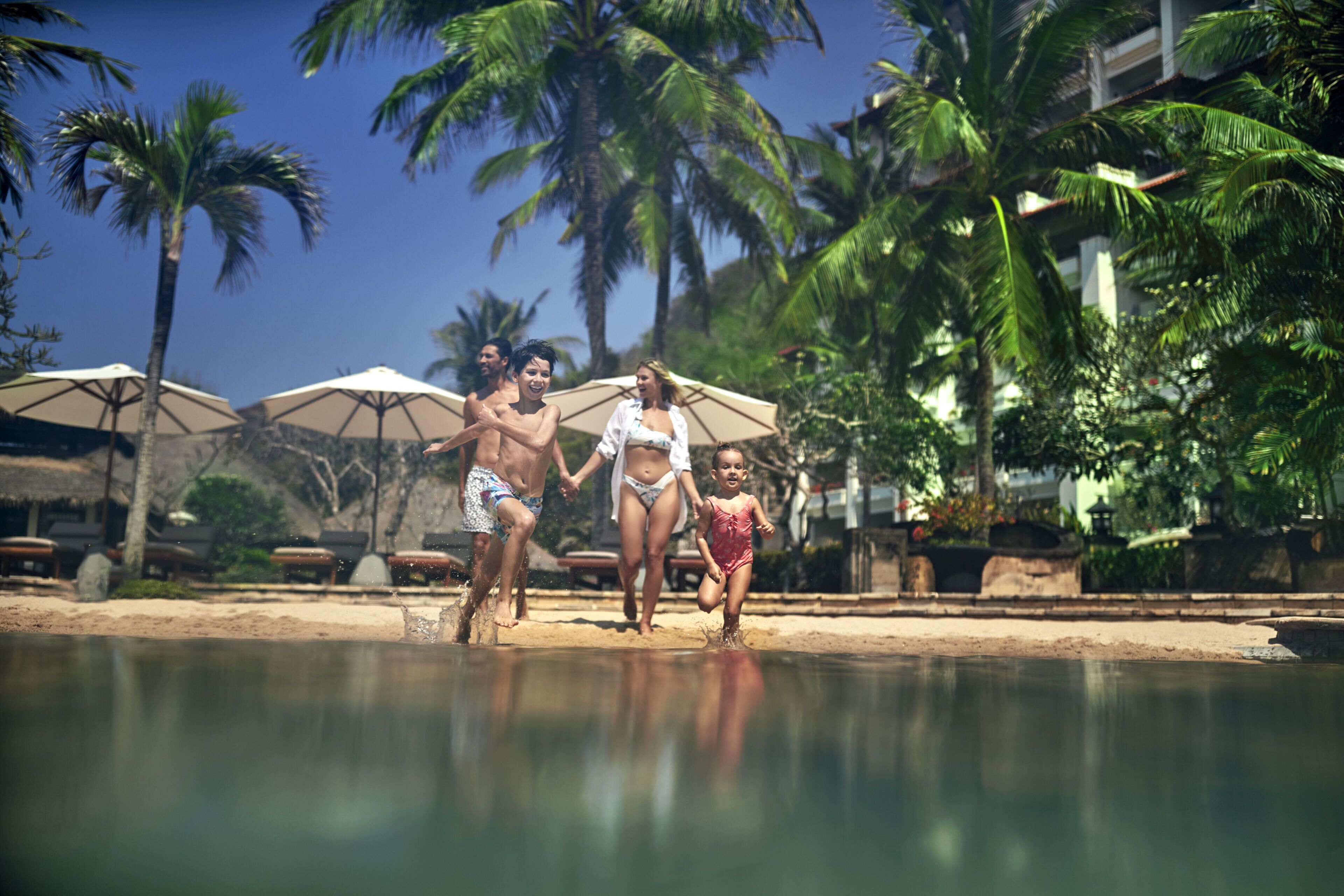 Un espace aménagé au bord de la piscine, avec des parasols et des palmiers.
