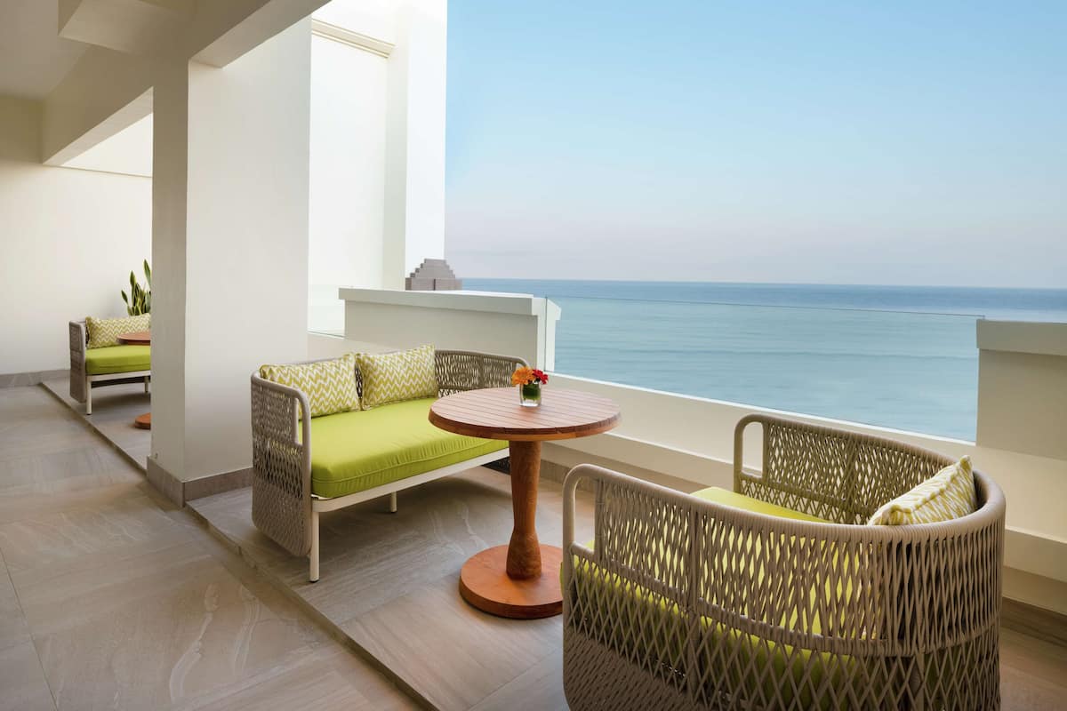 Ein Balkon mit Korbmöbeln, einem runden Holztisch und Blick aufs Meer.
