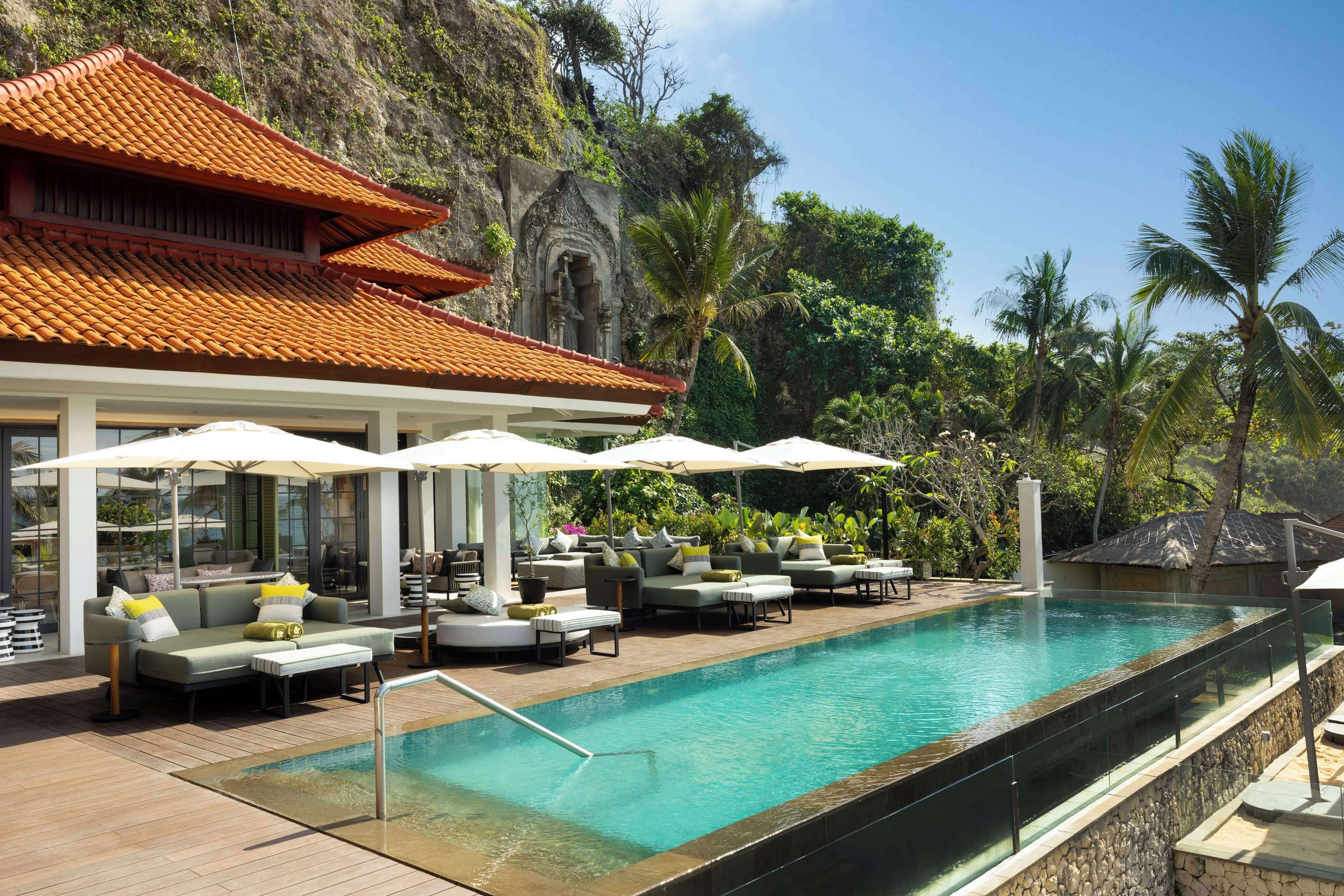 A poolside area with lounge chairs, umbrellas, and a traditional building with a tiled roof.