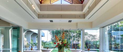 A modern hotel lobby with a high ceiling, large windows, and a central glass table displaying appetizers.