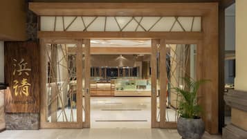 A hotel entrance with a wooden and glass facade, a reception desk, and a potted plant.