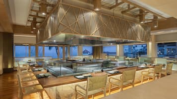 A modern restaurant with a long counter, wooden chairs, and a high ceiling with exposed beams.