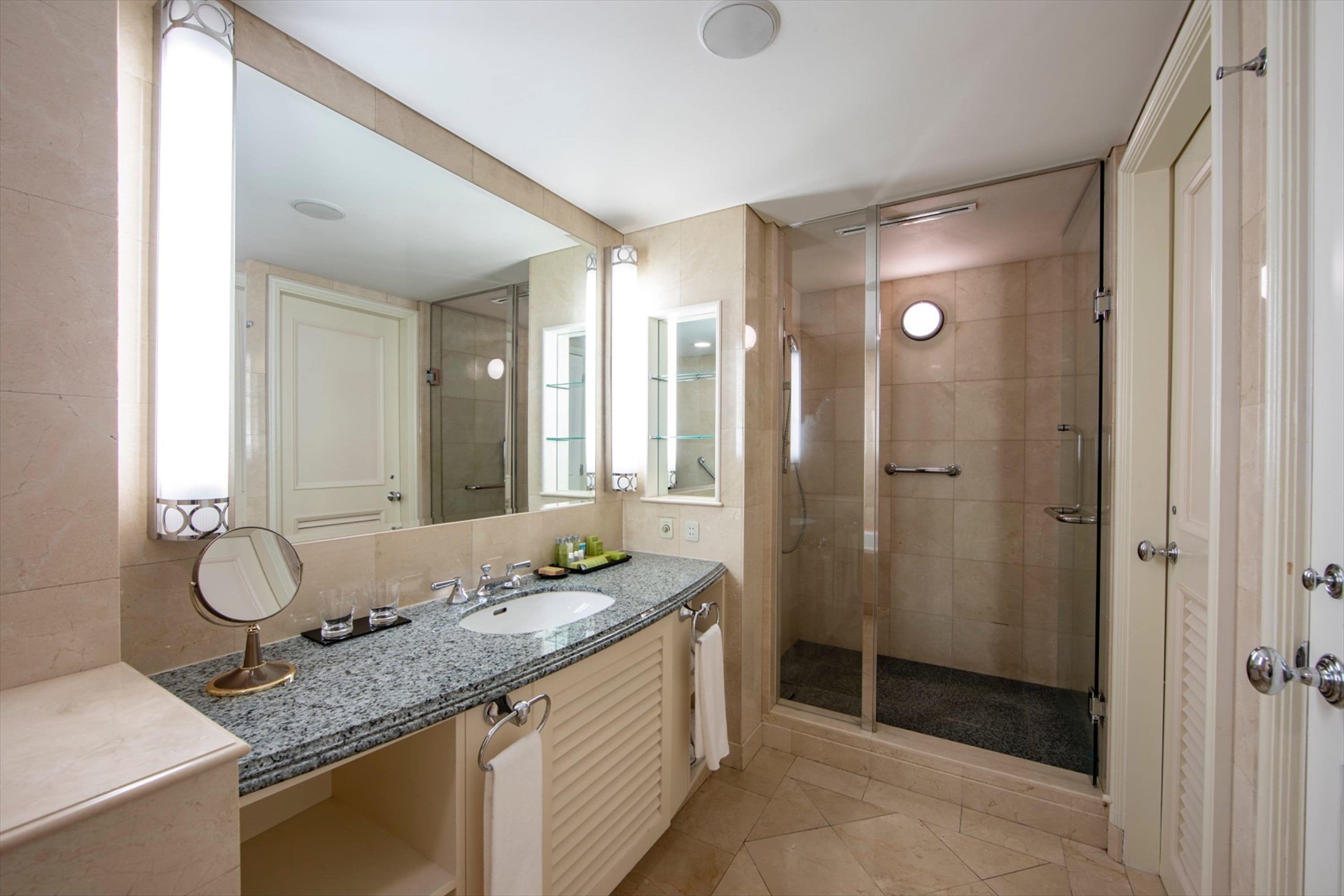 A bathroom with a granite countertop, a sink, a mirror, a glass shower enclosure, and a door.
