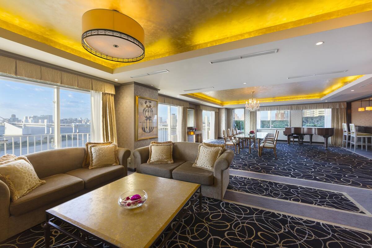 A hotel lobby with a sofa, a coffee table, a piano, and a view of the city.