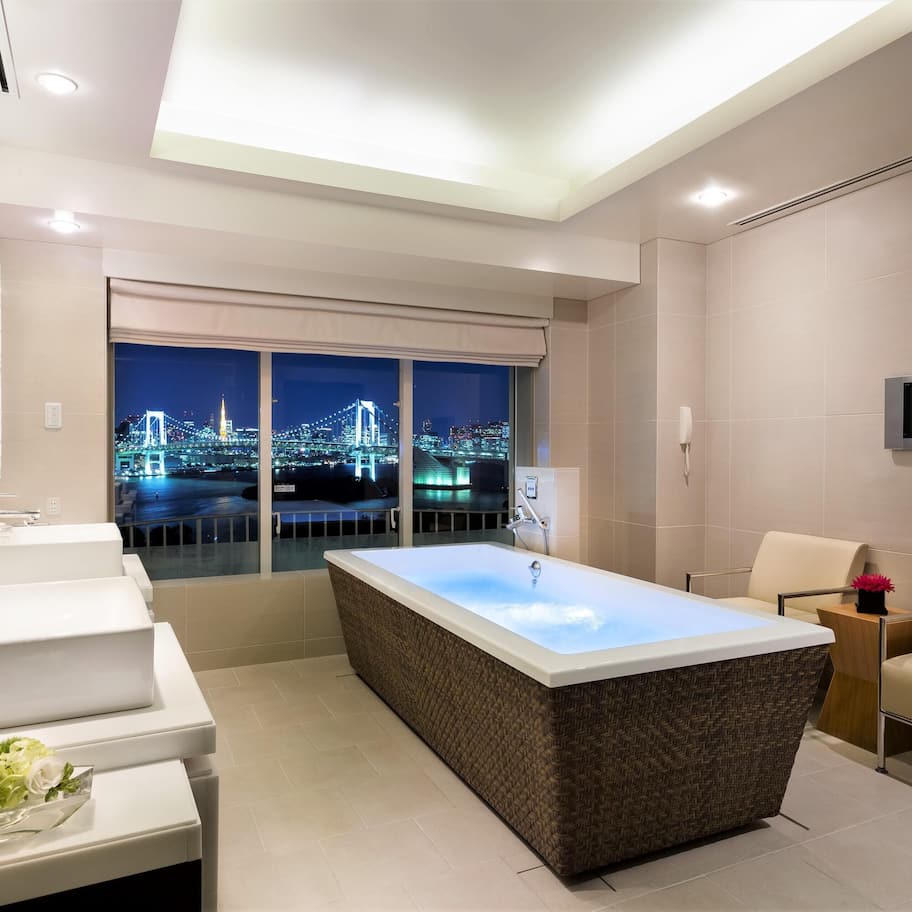 A modern bathroom with a large bathtub, a vanity with a mirror, and a television mounted on the wall.