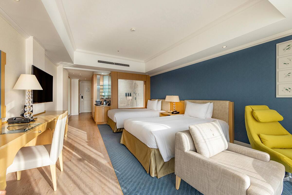A hotel room with a bed, two bedside tables, a desk with a chair, a TV, and a yellow chair.