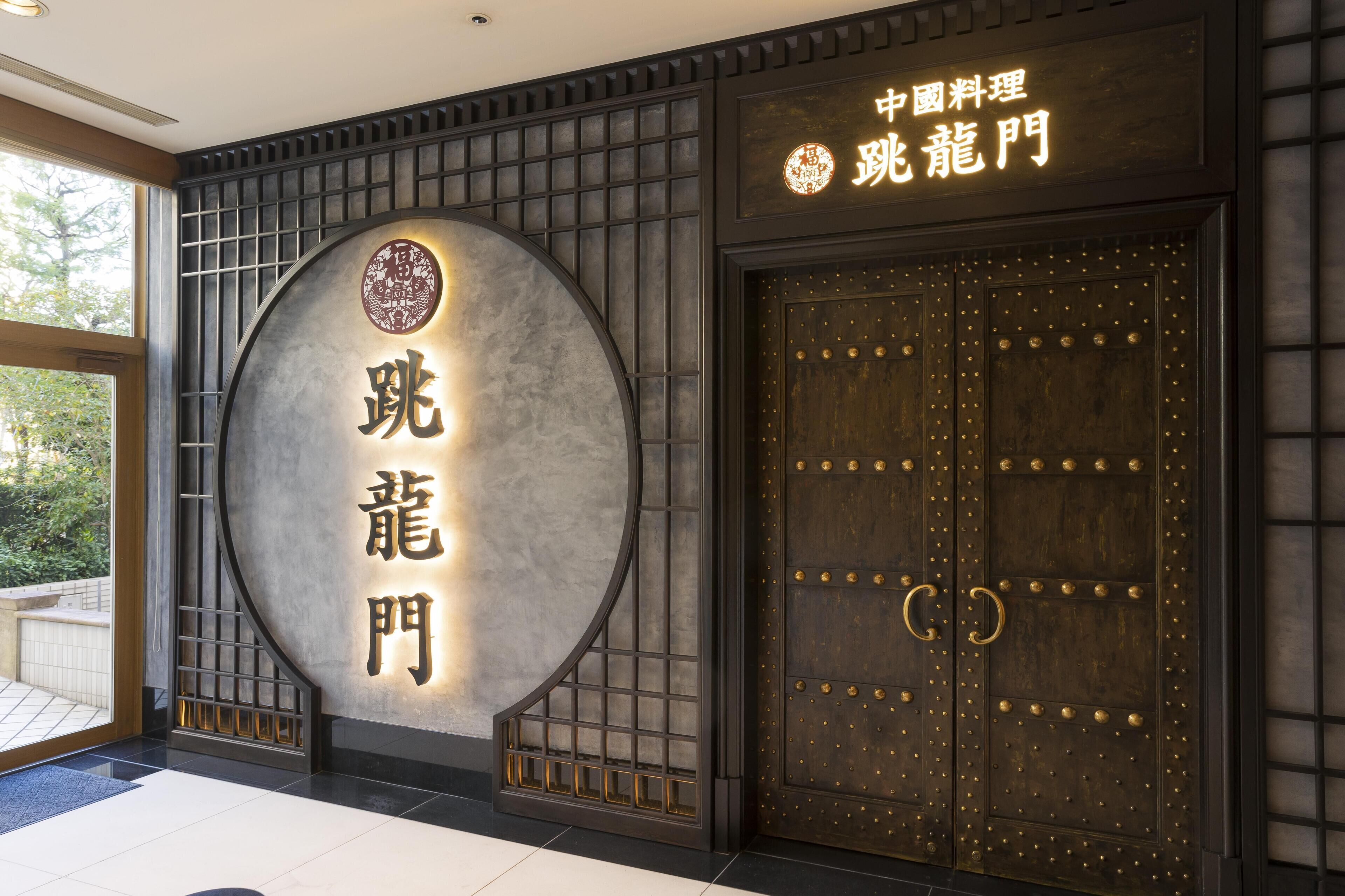 Entrada de construção tradicional chinesa, com uma placa circular e uma grande porta de madeira com tachas douradas.