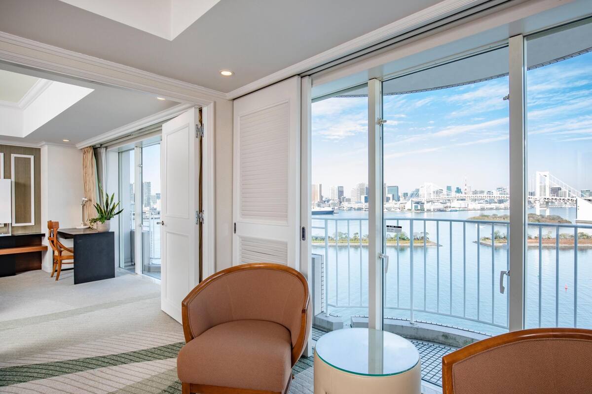 A hotel room with a city view, a balcony with a railing, a round table, and a chair.