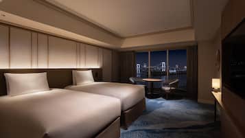 A hotel room with two beds, a view of a cityscape, a small table, and a chair.