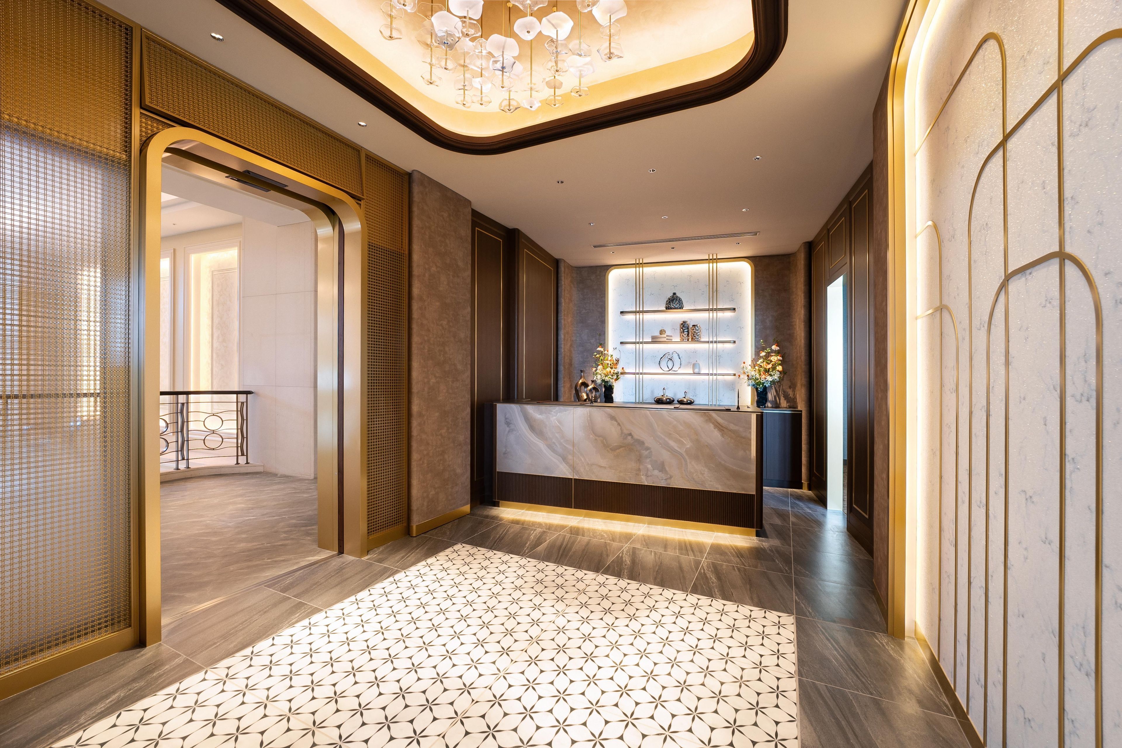 A modern hotel lobby with a reception desk, a patterned floor, and a decorative ceiling light.