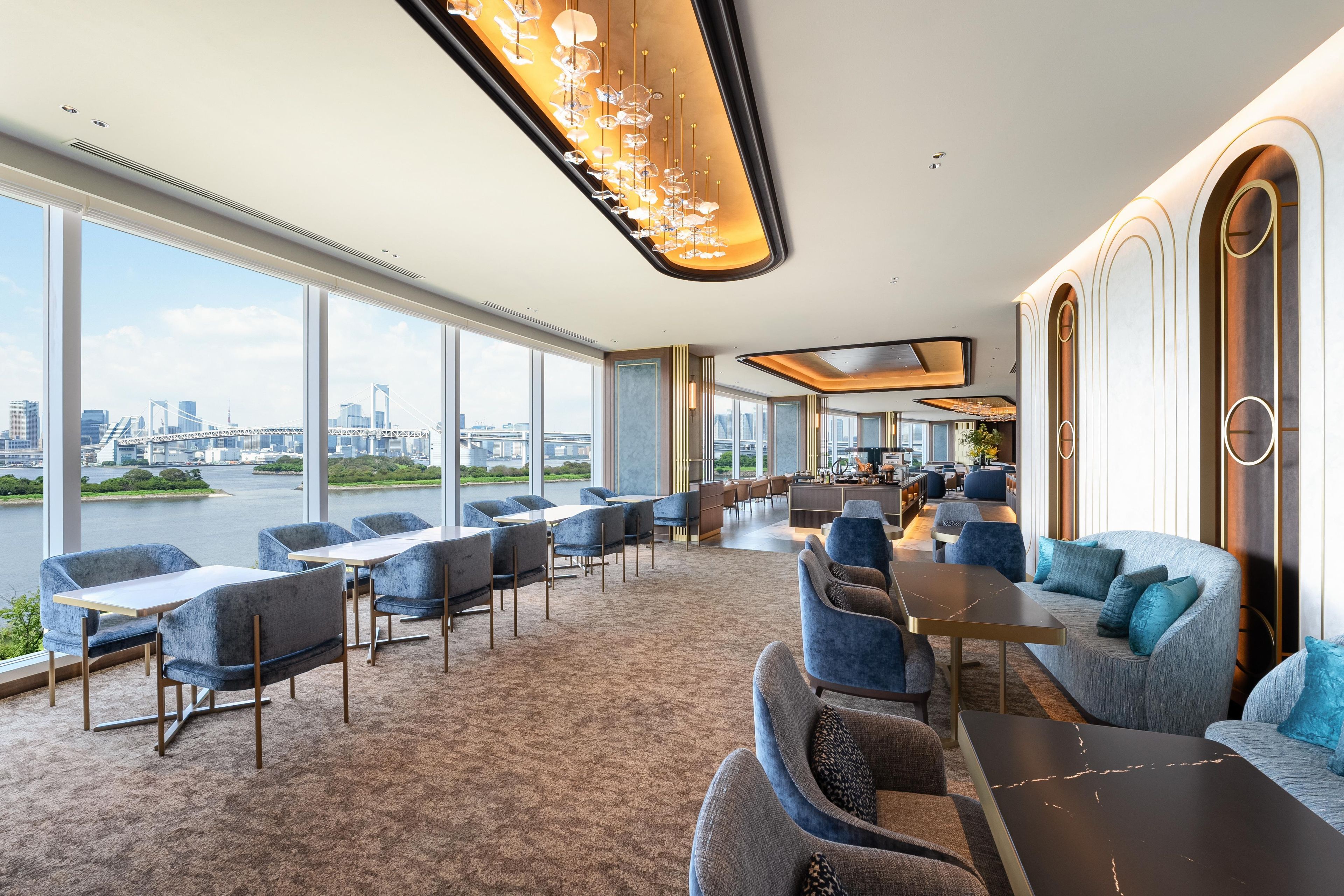 A spacious hotel lobby with a large seating area, a view of the cityscape, and a modern chandelier.