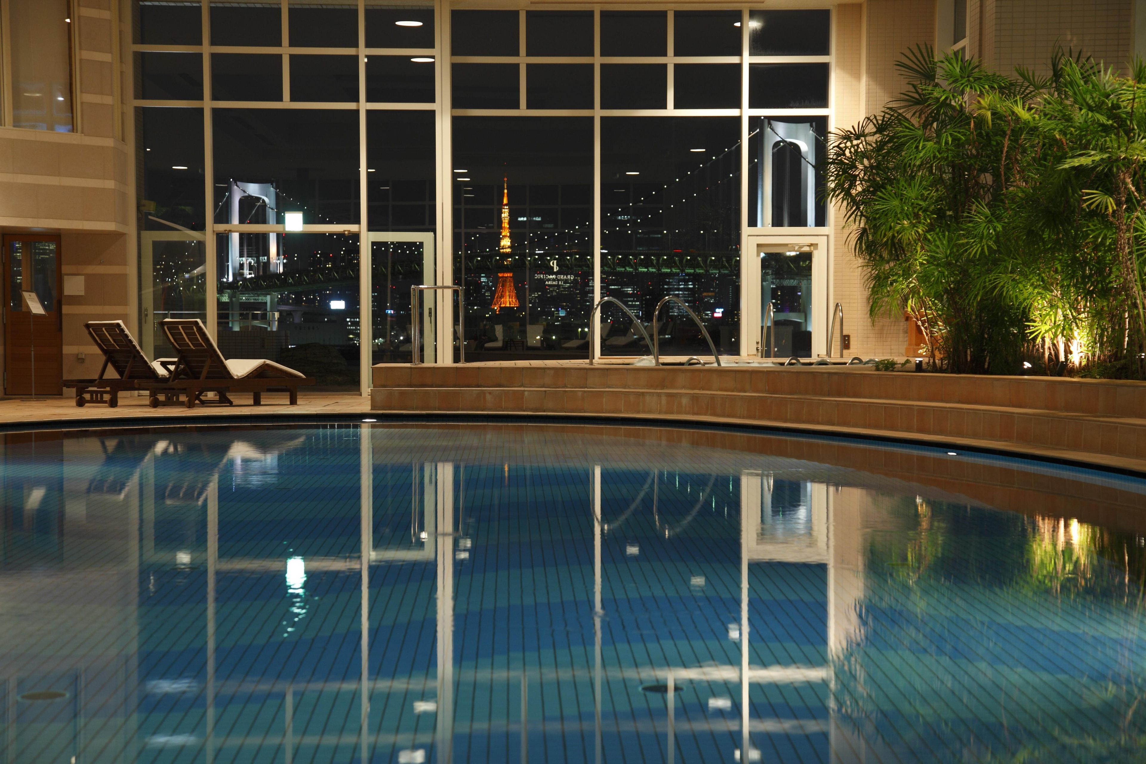 Una piscina con vistas a la ciudad, incluyendo una torre destacada, y sillas de descanso.
