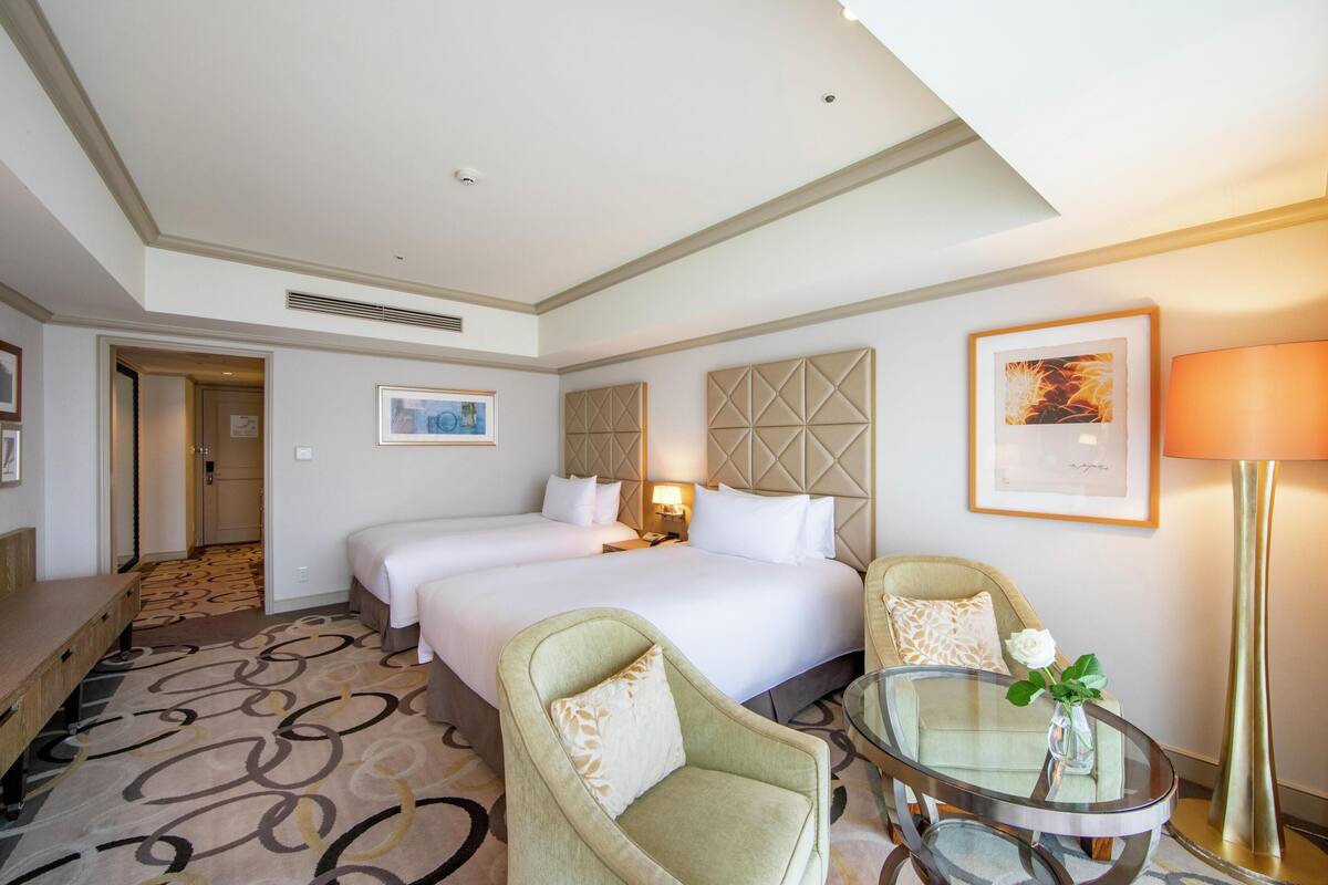 A hotel room with a large bed, two armchairs, a glass coffee table, a lamp, and a framed picture on the wall.