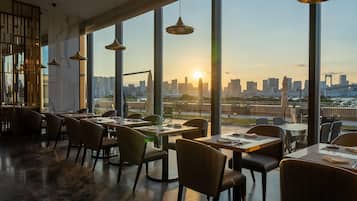 A restaurant with a city skyline view, modern furnishings, and pendant lighting.