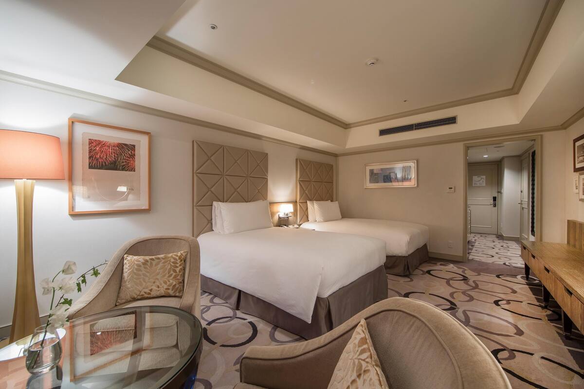 A hotel room with a double bed, a sofa, a glass table, and a lamp.