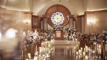 An aisle with candles and floral arrangements leading to a pulpit, with a stained glass window above.