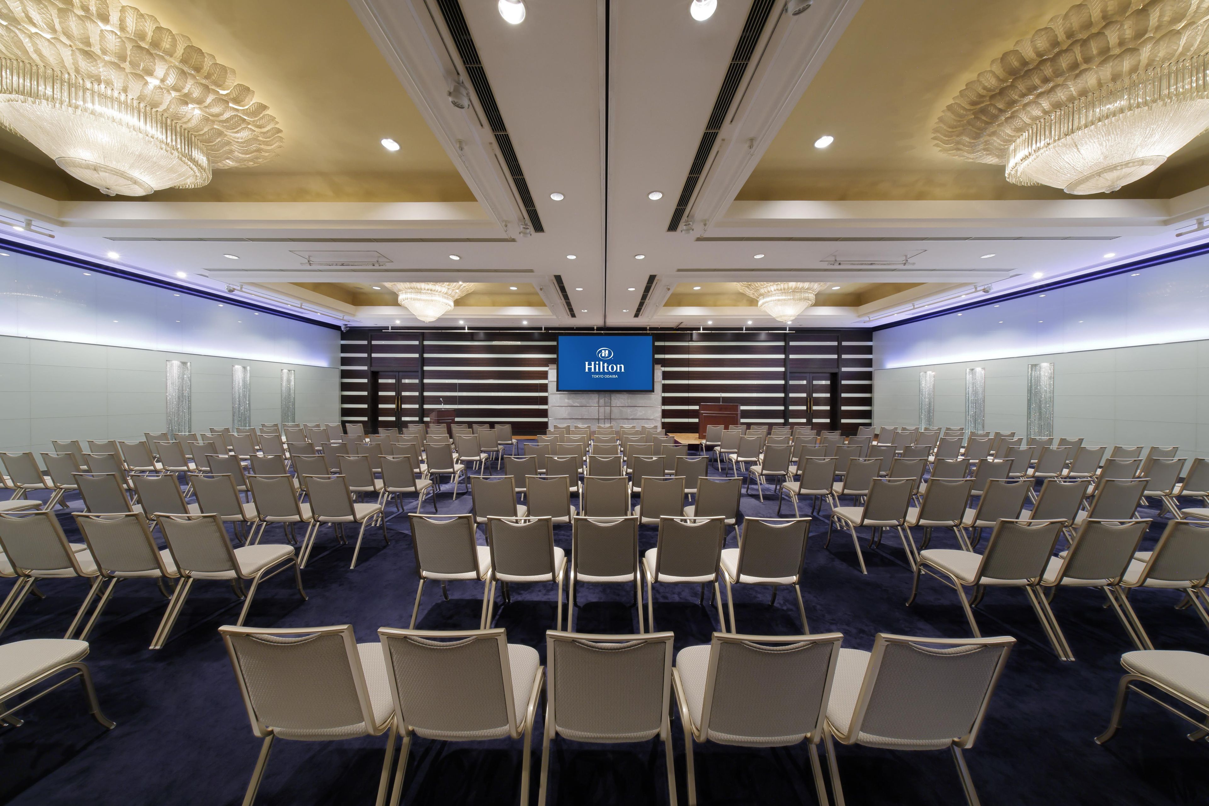 A hotel conference room with rows of chairs, a podium, and a Hilton sign.