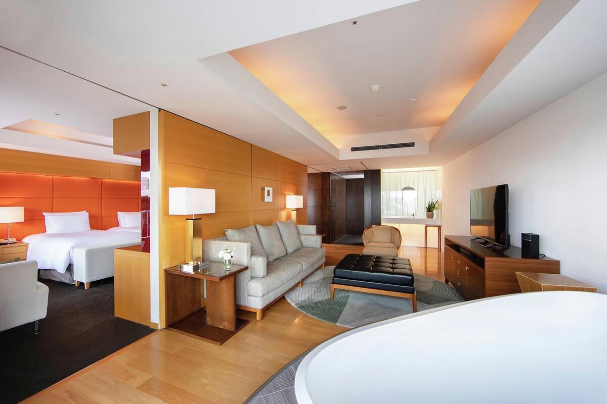 A modern hotel room with a bed, sofa, TV, and a desk with a lamp.