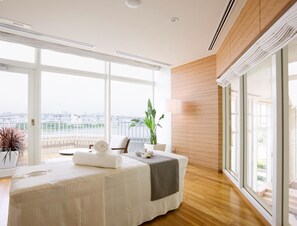A modern hotel room with a large bed, a sitting area, and a view of the cityscape.