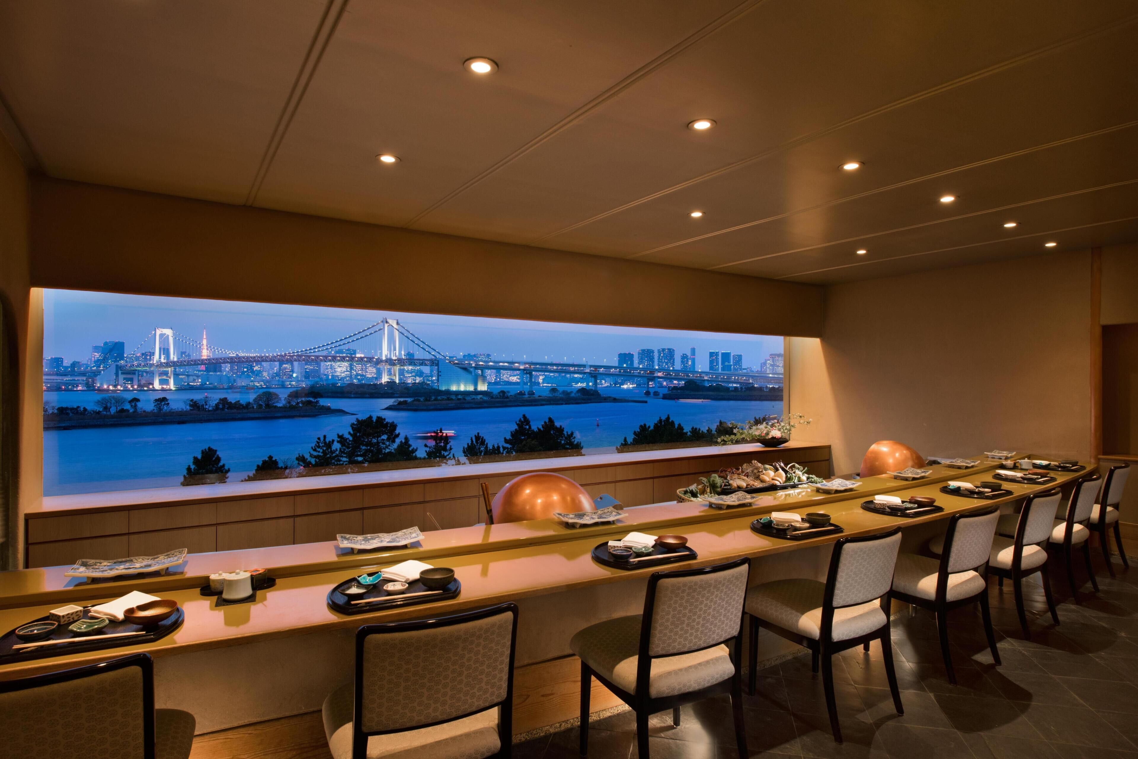 A modern bar area with a long counter, multiple chairs, and a large window with a cityscape view.
