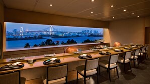 A modern bar area with a long counter, multiple chairs, and a large window with a cityscape view. - Hilton Tokyo Odaiba (Tokyo)