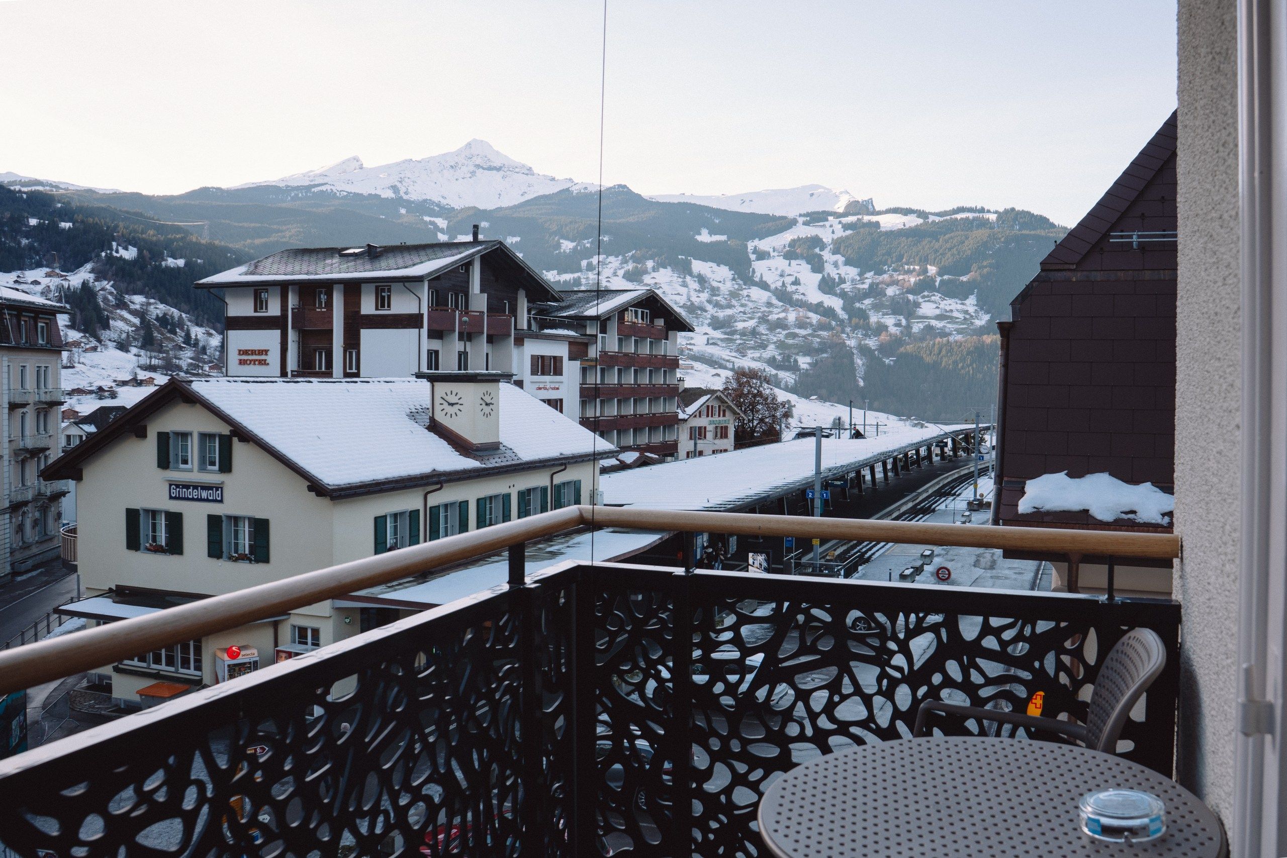 A balcony with a view of a mountain, a building with a sign 'Grindelwald', and a snow-covered landscape.