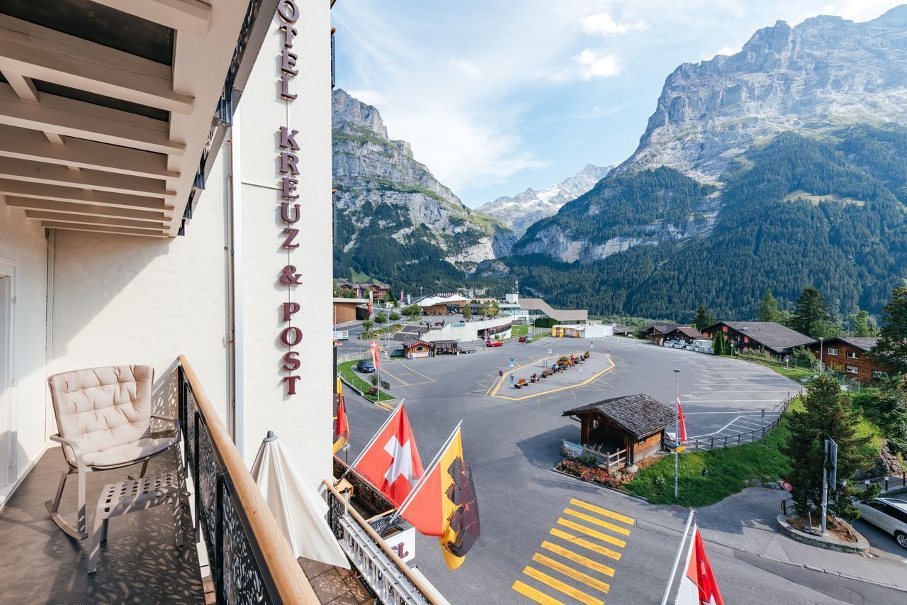 Das Hotel "Hotel Kreuz & Post" mit Balkon, Blick auf eine Berglandschaft und einem Parkplatz mit Flaggen.