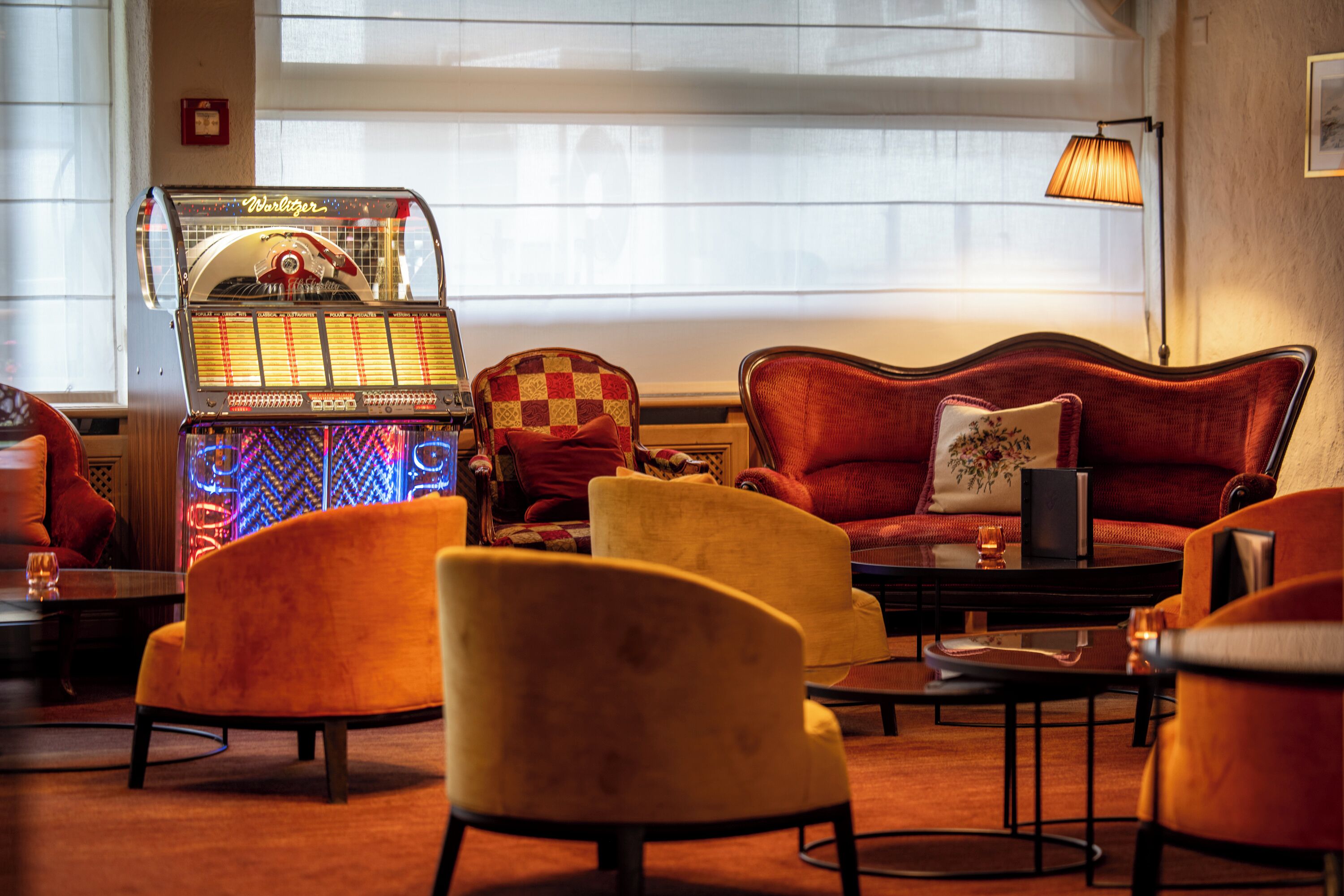 A cozy room with a jukebox, plush armchairs, a sofa, and a lamp.