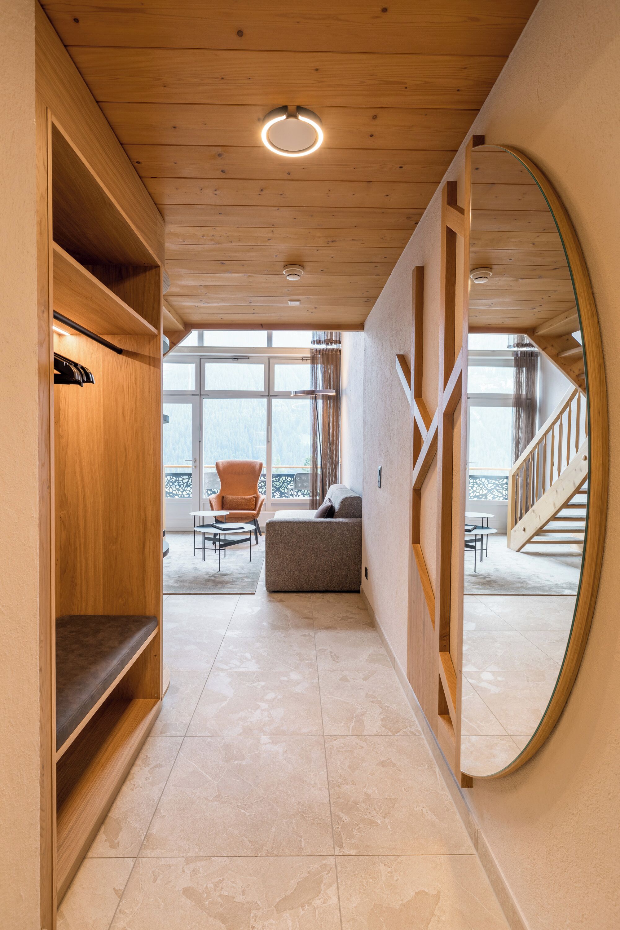 A hallway with a wooden ceiling, a round mirror, a sofa, and a chair.