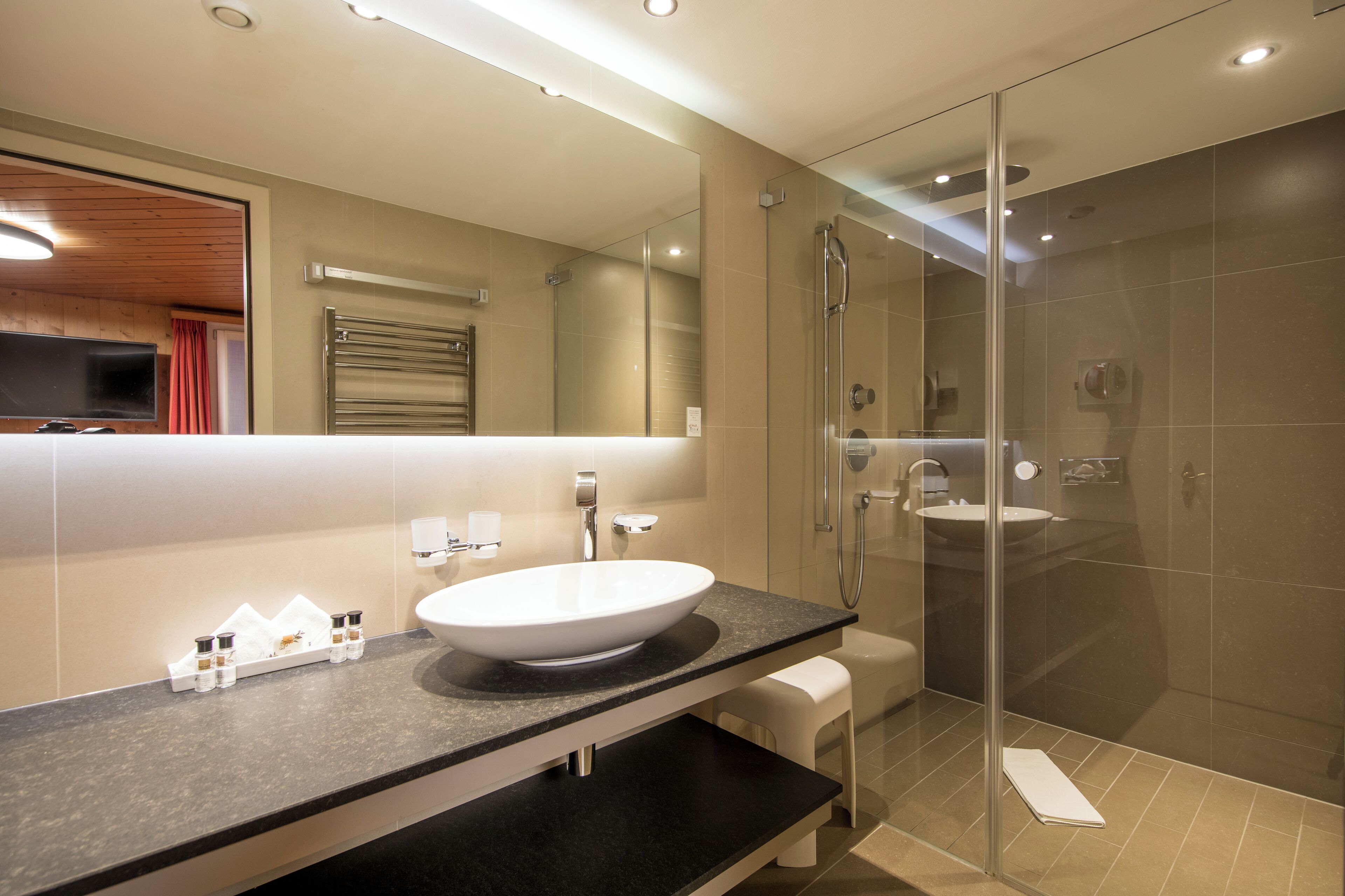 A modern bathroom with a large mirror, a round sink, and a glass-enclosed shower.