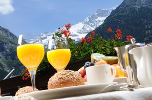 A breakfast setup with a mountain view, including a glass of orange juice, a cup, a muffin, and a fruit bowl. - Hotel Kreuz & Post (Grindelwald)