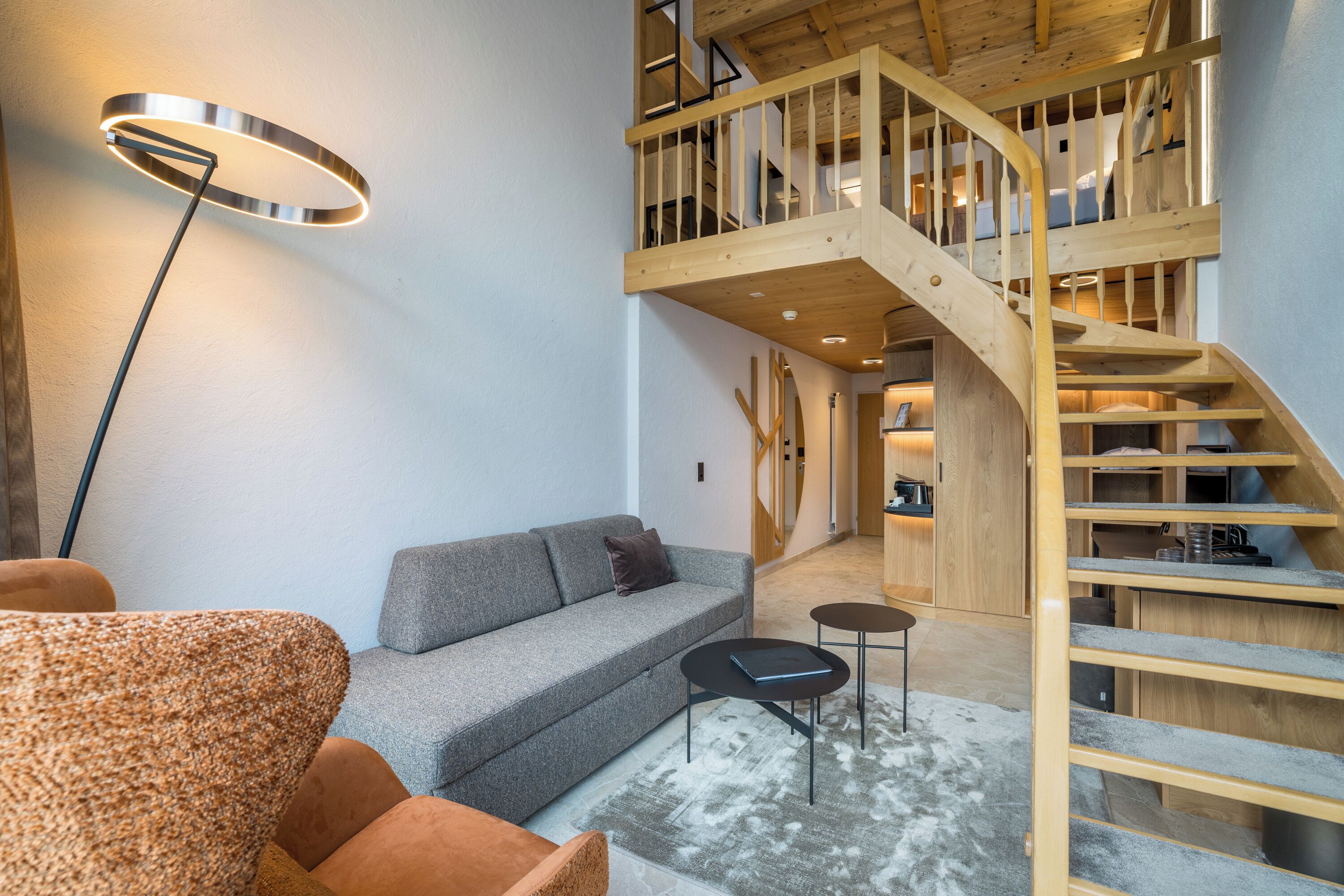 A modern interior with a grey sofa, a round floor lamp, and a wooden staircase leading to an upper level.