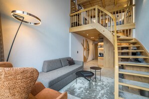 A modern interior with a grey sofa, a round floor lamp, and a wooden staircase leading to an upper level. - Hotel Kreuz & Post (Grindelwald)