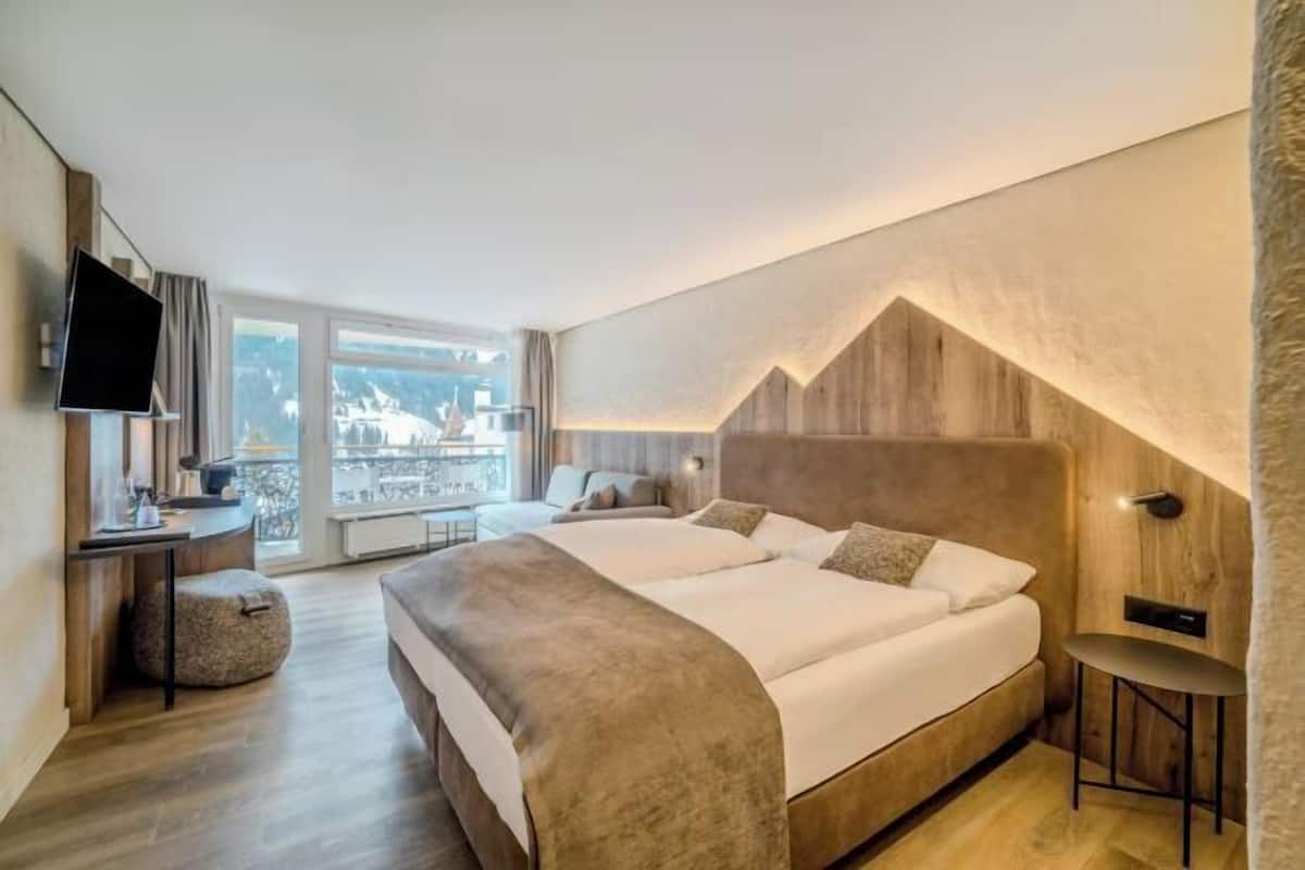 Ein modernes Hotelzimmer mit einem großen Bett, einem Fernseher, einem Schreibtisch und Blick auf die Stadt.