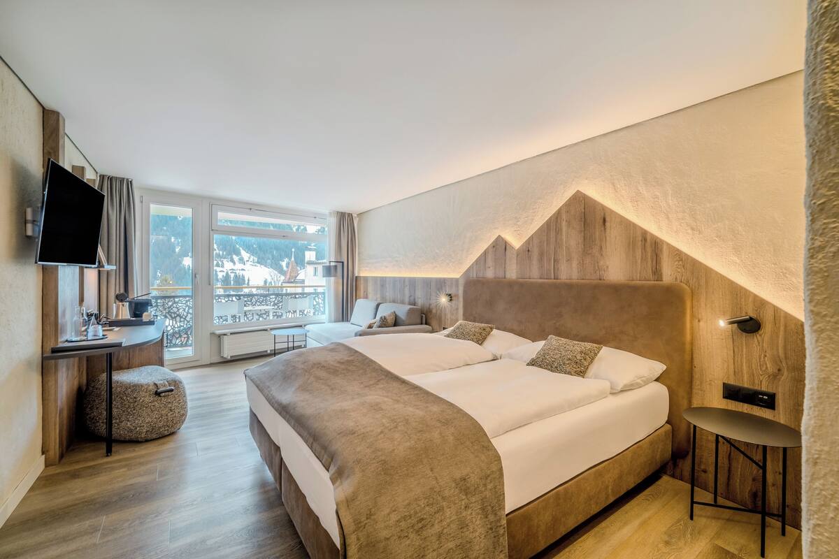 Ein modernes Hotelzimmer mit einem großen Bett, einem Schreibtisch, einem Fernseher und Blick auf die Berge.