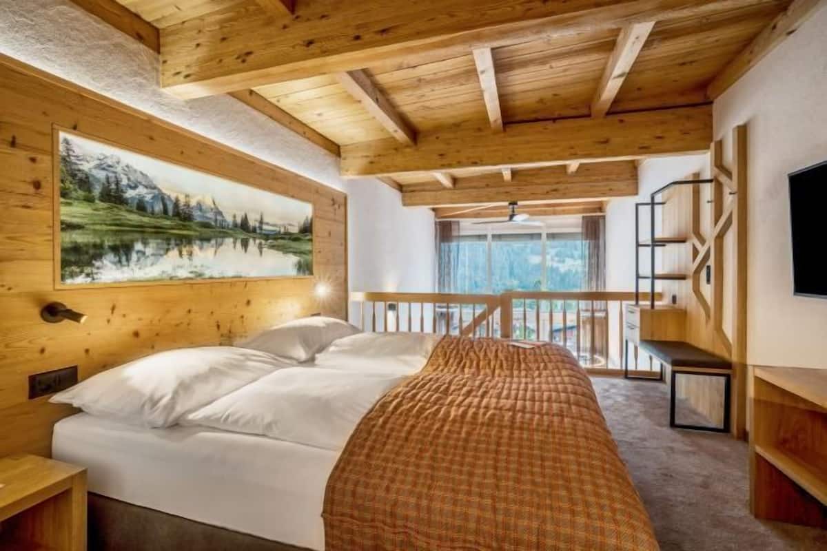 Ein Schlafzimmer mit Holzboden, einem Bett mit weißer Bettwäsche, einem Gemälde von einer Berglandschaft und einem Balkon mit Aussicht.