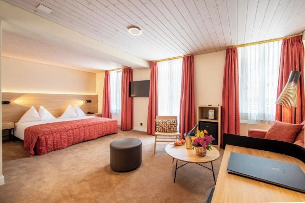 A hotel room with a bed, a desk, a chair, a TV, and a window with curtains.
