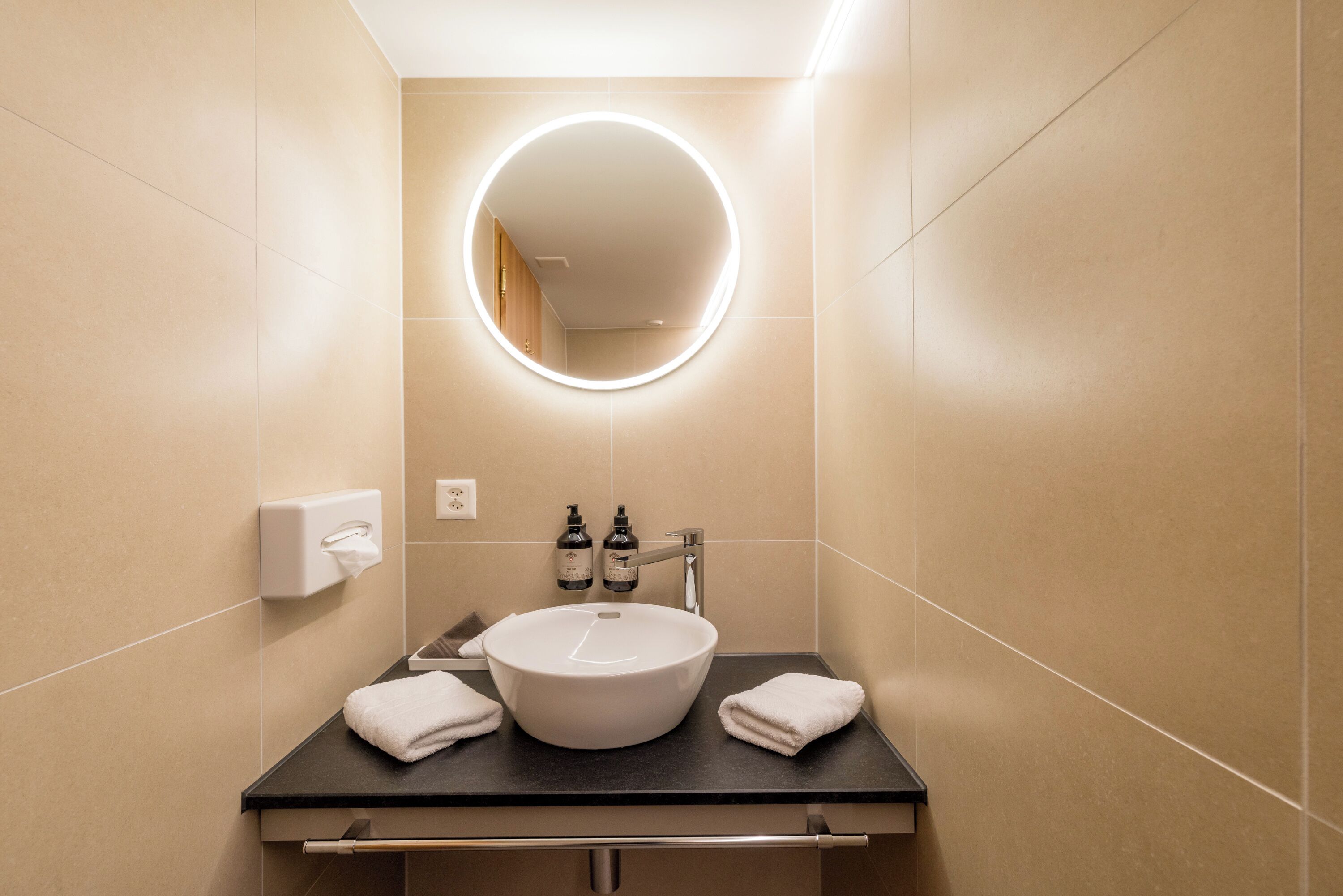 Un baño moderno con un espejo redondo, un lavabo blanco y dos botellas de champú.
