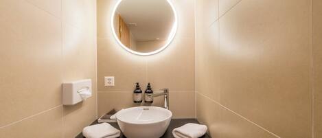 Un baño moderno con un espejo redondo, un lavabo blanco y dos botellas de champú.