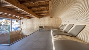 A modern spa room with wooden ceiling beams, a glass wall, and a seating area with cushions. - Hotel Kreuz & Post (Grindelwald)
