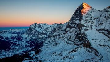 A snow-covered mountain peak at sunset with rugged terrain and rocky outcrops.