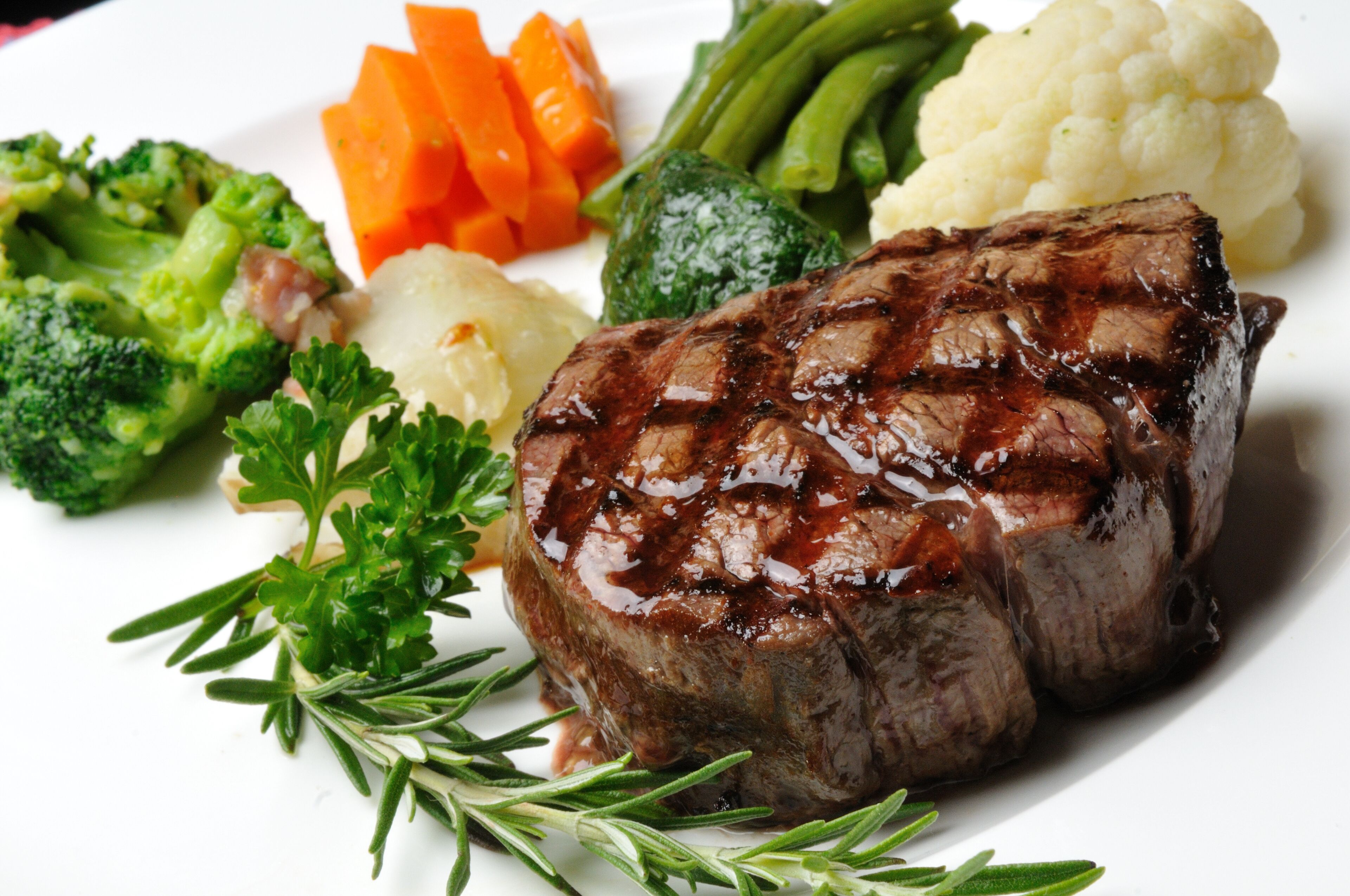 A plate with a grilled steak, broccoli, carrots, green beans, cauliflower, and parsley.