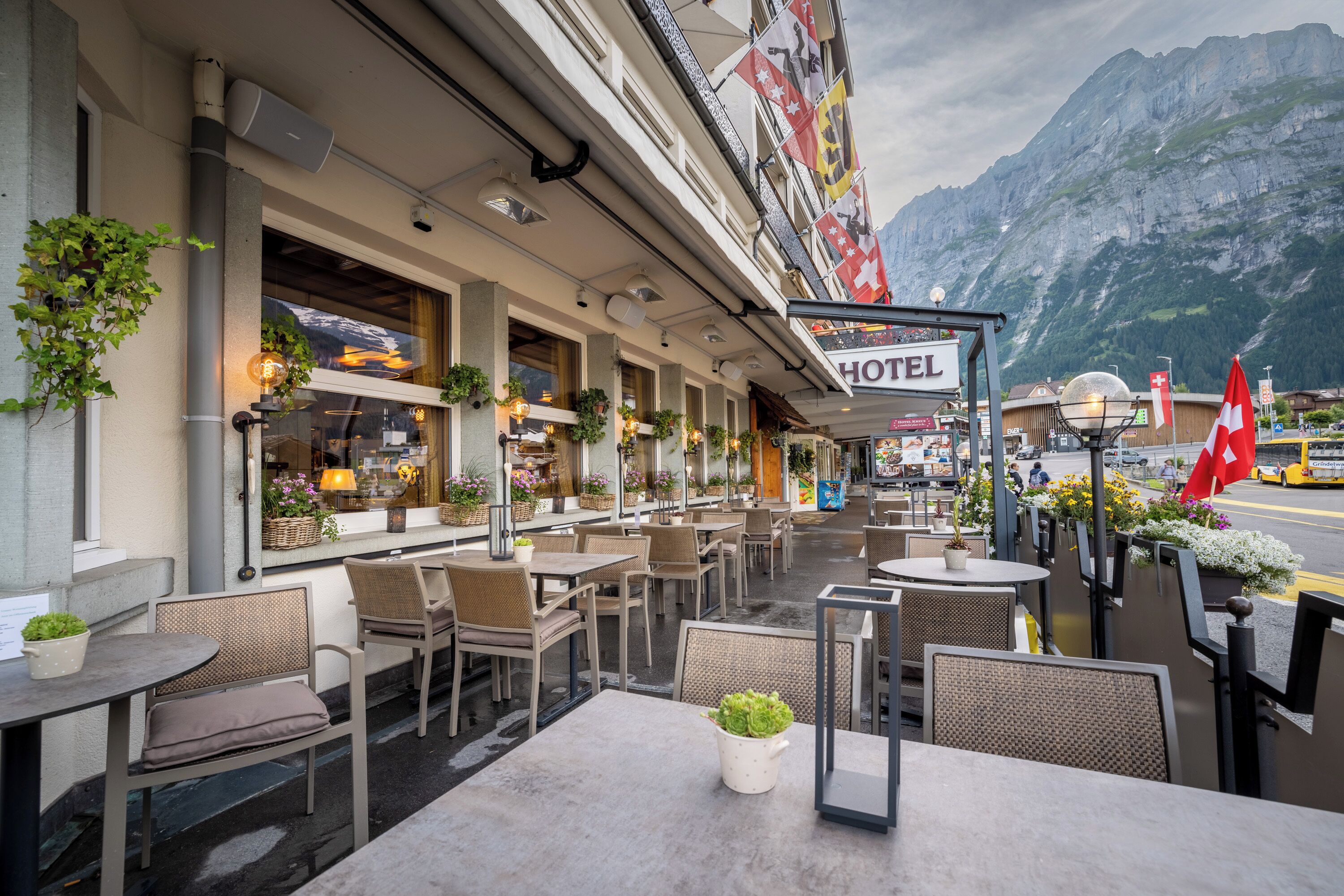 Een terras van een hotel met tafels en stoelen, plantenpotten en een berg op de achtergrond.