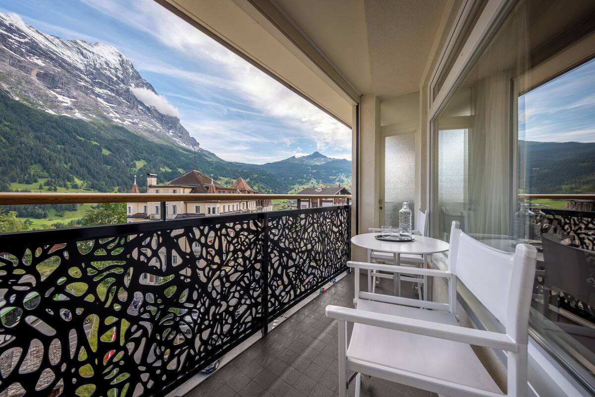 Ein Balkon mit Blick auf Berge, weißen Stühlen und einem Tisch.