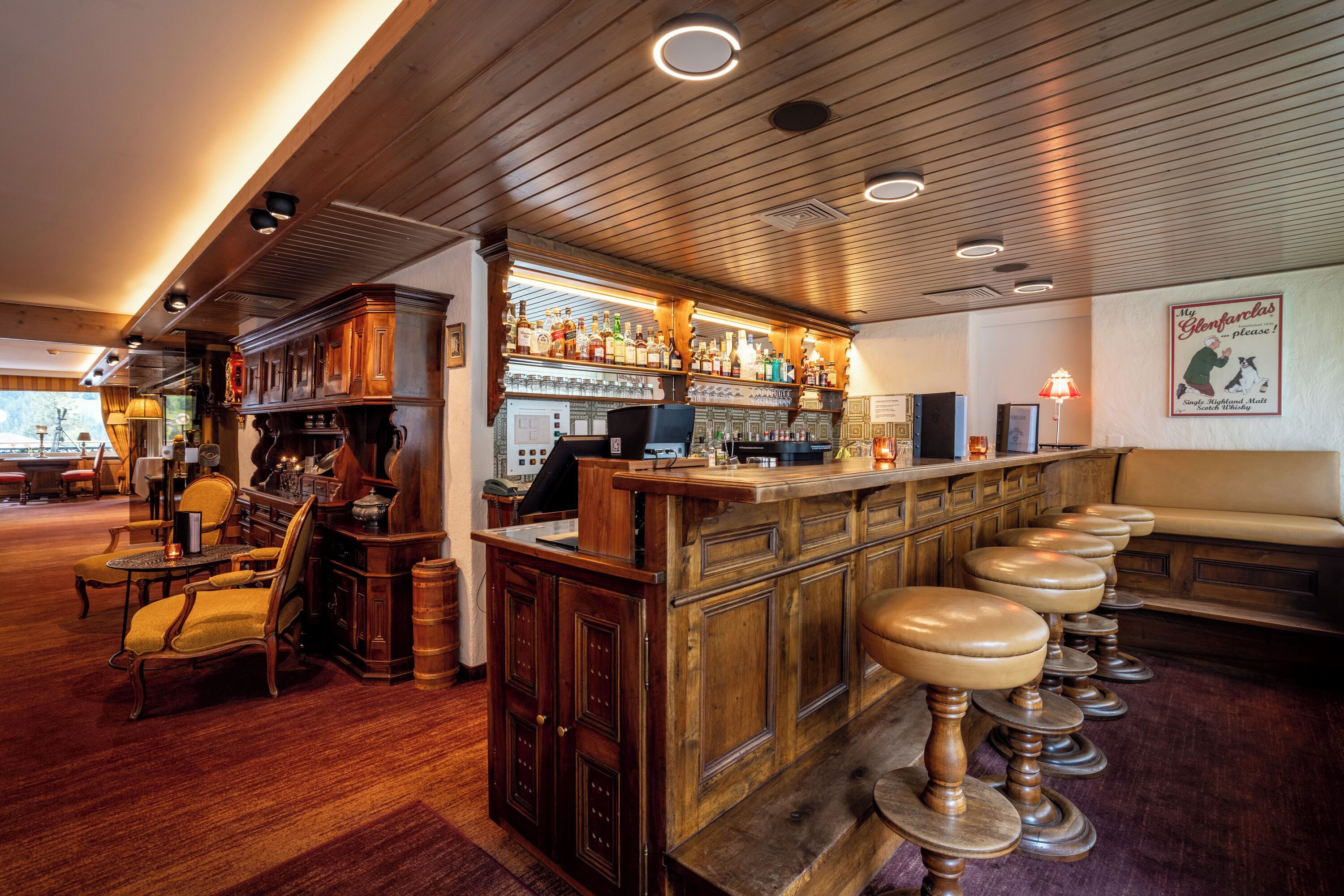 A bar area with wooden bar stools, a counter with bottles, and a seating area with a couch.